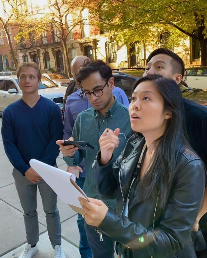 Team solving clues during a Greenwich Village scavenger hunt, gathered on a tree-lined brownstone block in Manhattan