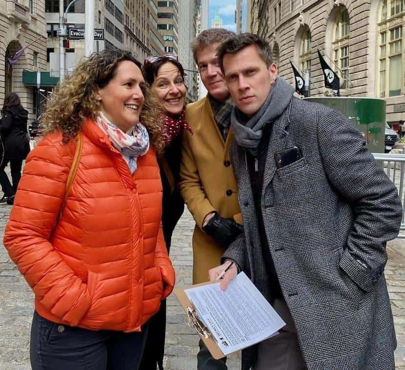 Small group posing with a clipboard during a scavenger hunt at Evacuation Day Plaza near the Charging Bull in Lower Manhattan
